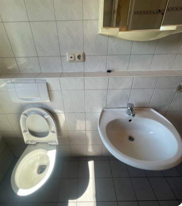 Dasselbe Waschbecken mit WC nach der Reinigung: weiße Keramik, saubere Fliesen