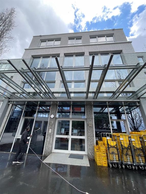 Mitarbeiter reinigt die Glasfassade eines mehrstöckigen Bürogebäudes mit einer wassergeführten Teleskopstange vom Boden aus