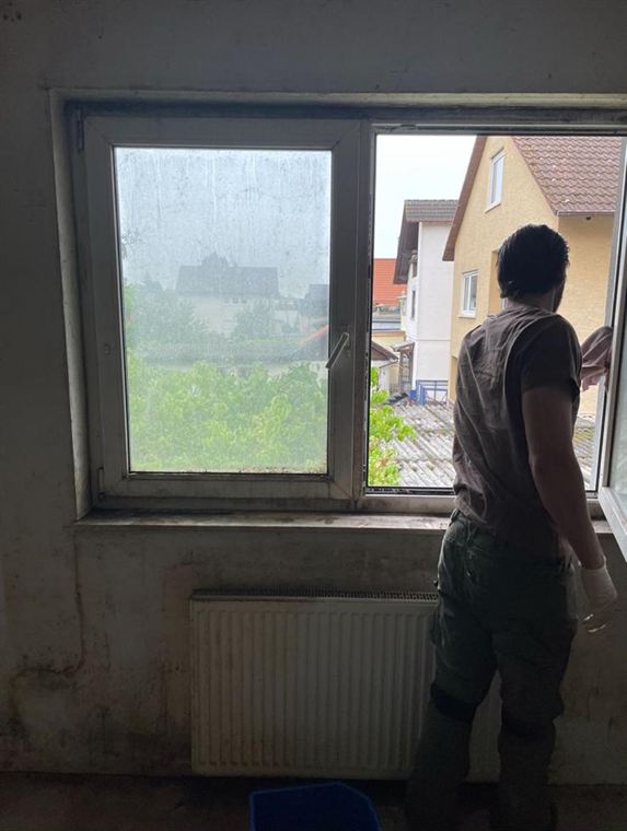 Mitarbeiter bei der Fensterreinigung in einem leerstehenden Raum: links eine noch blinde Scheibe, rechts der geöffnete Fensterflügel