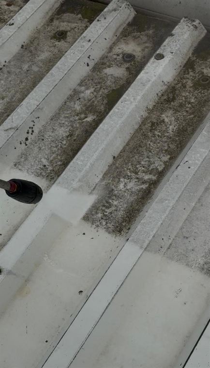 Trapezblechdach während der Hochdruckreinigung: links eine blitzsaubere Bahn, rechts daneben noch Moos und Verschmutzung