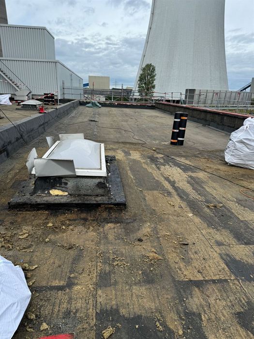 Abgetragenes Flachdach eines Industriegebäudes, im Hintergrund ein Kühlturm, daneben Bigbags mit Dämmmaterial